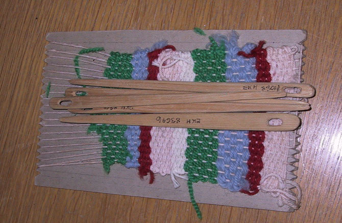 Hjemmelaget vev med pinner. Kartongplate, hyssing som renning og ulltråd som vev.