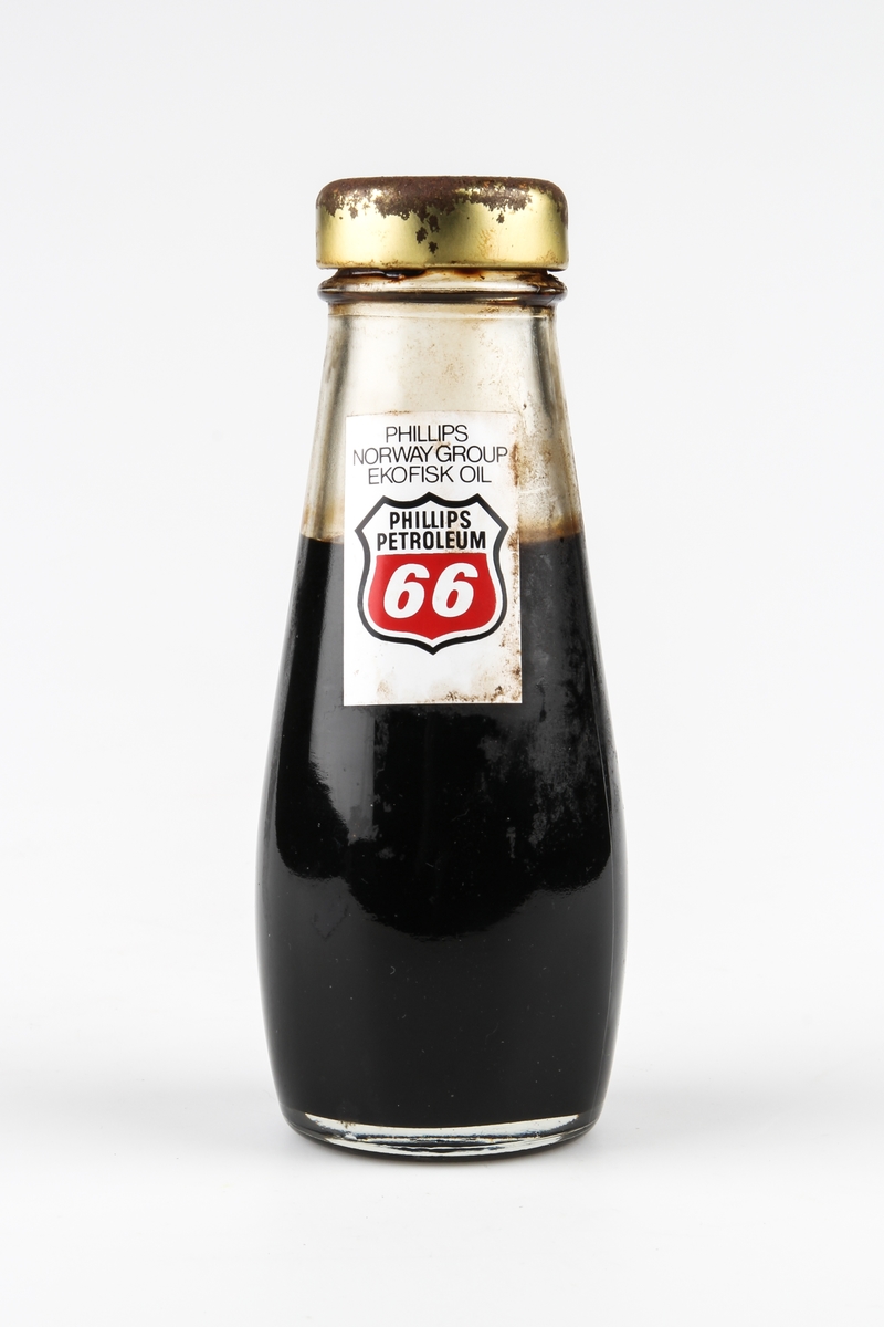 Oljeprøve fra Ekofisk oppbevart i en flaske med skrukork. På ene siden er merkelapp med Phillips Petroleums logo. På den andre siden er merkelapp med Offshore North Sea (ONS) 1974.