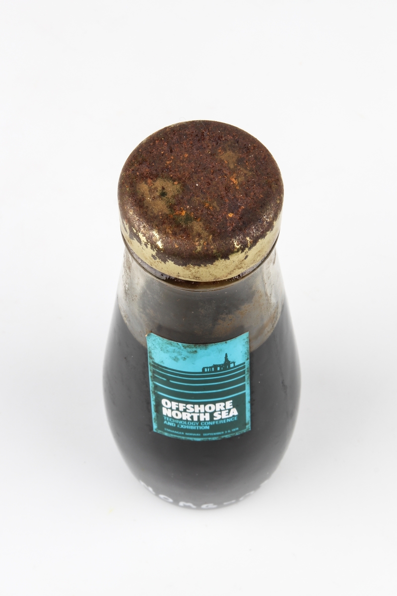 Oljeprøve fra Ekofisk oppbevart i en flaske med skrukork. På ene siden er merkelapp med Phillips Petroleums logo. På den andre siden er merkelapp med Offshore North Sea (ONS) 1974.