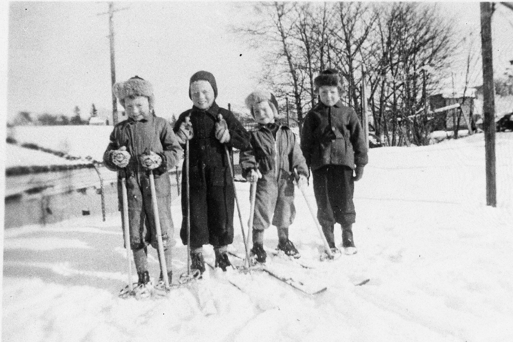 Barn på ski. Dei står på eigendomen til John Stensland lengst vest i Storgata der det nå (i 1990) er parkeringplass, vis a vis Helland Matsenter. I bakgrunnen Bryneåna og Brynehaugen. Sjå også 1990.1TIM.27.012 og 1990.1TIM.27.014.
Frå v. Jon Stensland, Tor Bolme, Steinar Stensland, Åsmund Moi (bror til Tollef Moi)