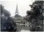 Norberg sn, Norberg.
Norbergs kyrka i bakgrunden, med å och byggnader i förgrunden.