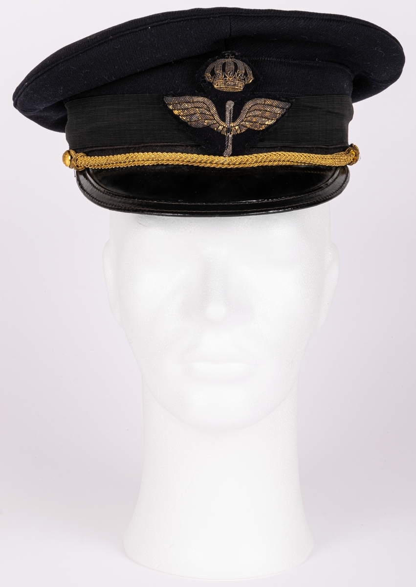 Skärmmössa m/30 för flygvapnet.
Av mörkblått ylletyg (gabardin) med svartlackerad skärm (undersidan ljusgrön). Svart textilband runt mössans nederdel. Kullen cirkelrund, platt och med större diameter. Dess styvnader är borttagna. Flygemblek av broderad guldtråd. Hakrem av flätad guldtråd (m/39), fäst med två små kronknappar. Vitt linnefoder. Svettremmen märkt "HF". etikett i kullen "KÖRSNÄR Lundbladhs HÄLSINGBORG"