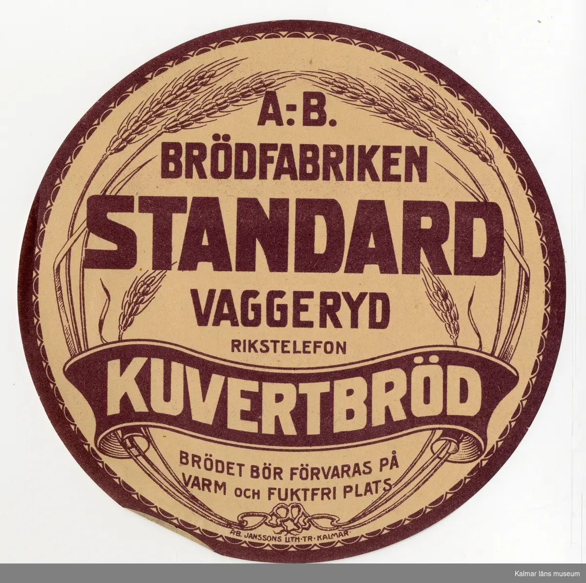 KLM 21360:3:28 Etikett, av papper, tryck av litografisk etikett. På etiketten text: Standard Kuvertbröd. I färgen brun text på beige bakgrund. Etikett till knäckebrödsförpackning. Beställare: A.-B. Brödfabriken, Vaggeryd. Tryckt på Janssons Litografisk tryckeri i Kalmar. Trycket låg löst i provbok med varuetiketter mm, KLM 21360:1.