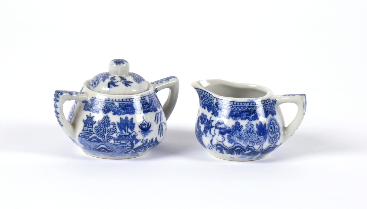 Dukkeservise i 12 deler; 6 tekopper og kanne, 2 kaffekopper og kanne, fløtemugge og sukkerskål. Dekoren har mønster i blått og hvitt; det populære "willow pattern" eller piletremønsteret.