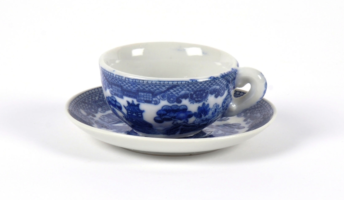 Dukkeservise i 12 deler; 6 tekopper og kanne, 2 kaffekopper og kanne, fløtemugge og sukkerskål. Dekoren har mønster i blått og hvitt; det populære "willow pattern" eller piletremønsteret.