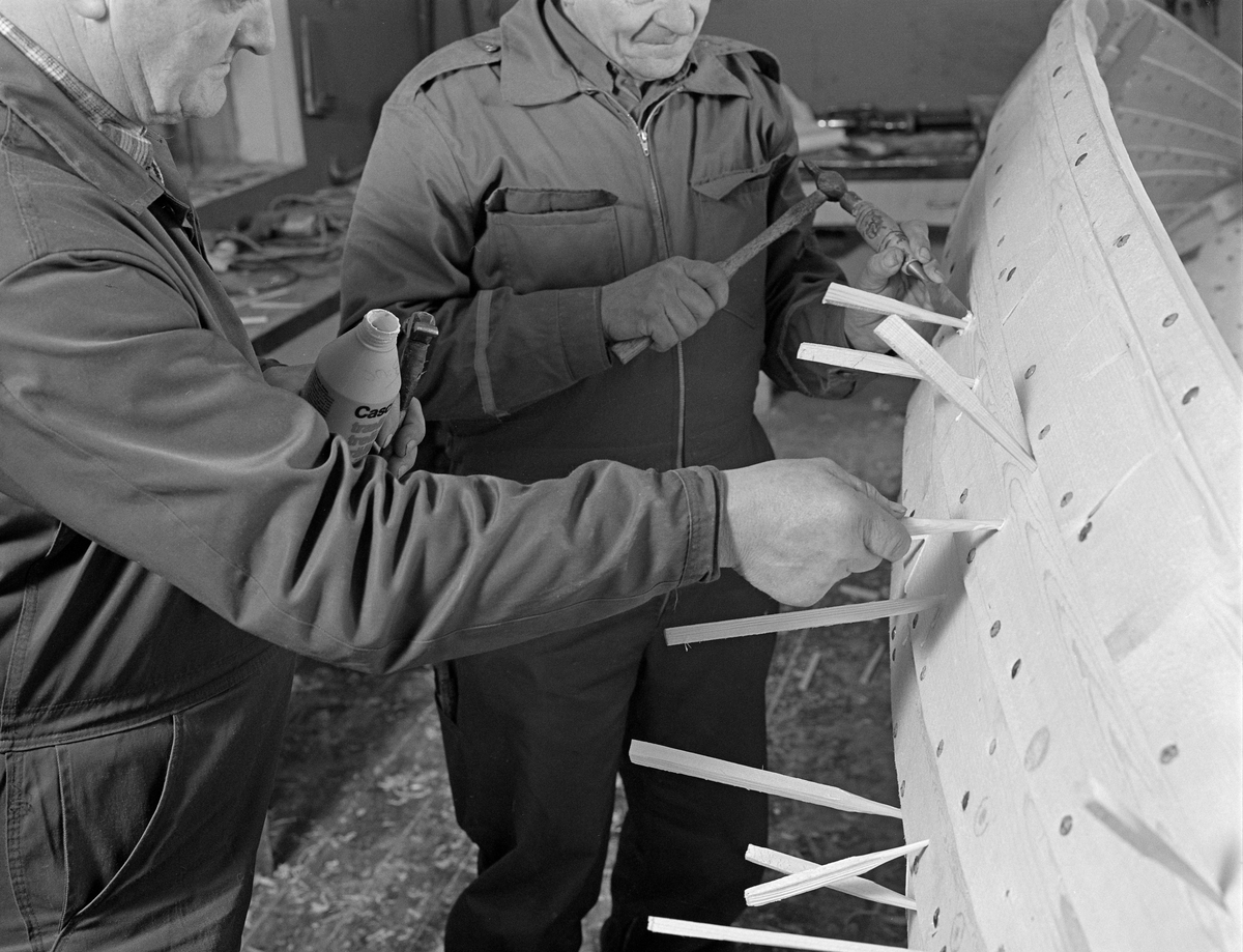 Bygging av fløterbåt («Flisa-båt») i Glomma fellesfløtingsforenings verksted på Breidablikk i Åsnes i november 1984. På dette fotografiet ser vi Lars Bernhard Olastuen og Johan Isaksætre banke treplugger inn i bordgangene. At dette var nødvendig skyldtes antakelig at det var svartkvist i materialene. Dette er kvistved som var død, og følgelig ikke lenger hadde noe vekstsamband med omkringvoksende stammeved da treet ble hogd. Det innebar fare for lekkasjer. Båtbord skulle derfor, i likhet med tønnestav, helst ikke ha for mye svartkvist.