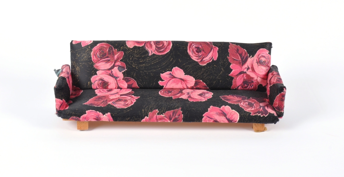 Dukkemøbler, sofa, bord og to stoler. Sofa og stoler er polstret og trukket med blomstret trekk. Bord av lakkert kryssfiner.