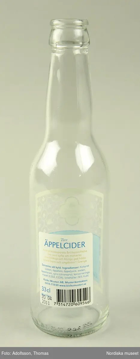 Flaska av klart glas. För äppelcider från Kiviksmusteri. 33cl 2,2% vol. etiketter av plast. Framtill etikett i blått och transparent med mönster från "Den officiella bröllopsserien" stiliserad krona och stjärna. Baktill vit etikett med text.

Text på etiketten framtill "2010 Den Officiella Bröllopsserien The Official Wedding Series","Torr ÄPPELCIDER Från hjärtat av Österlen Säljes till förmån för Kronprinsessparets Bröllopsstiftelse vars syfte är att motverka utanförskapet och främja god hälsa bland barn och ungdomar i Sverige. 2,2%vol. Kiviks MUSTERI 33cl" 
Text på etiketten baktill: "Torr Äppelcider Kronprinsessparets Bröllopsstiftelse har som syfte att motverka utanförskapet och främja god hälsa bland barn och ungdomar i Sverige. Serveras väl kyld. Ingredienser: [...] Kiviks Musteri AB Musterikontakten: 0414-71900 www.kivicksmusteri.se 33cl Bästföre: 20 04 2011.
/Johanna Krumlinde 2012