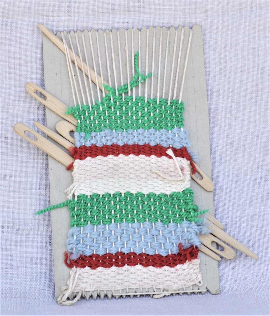 Hjemmelaget vev med pinner. Kartongplate, hyssing som renning og ulltråd som vev.