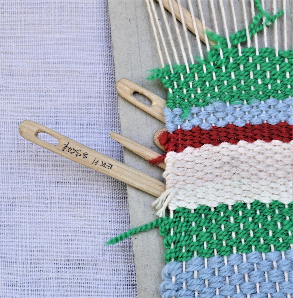 Hjemmelaget vev med pinner. Kartongplate, hyssing som renning og ulltråd som vev.