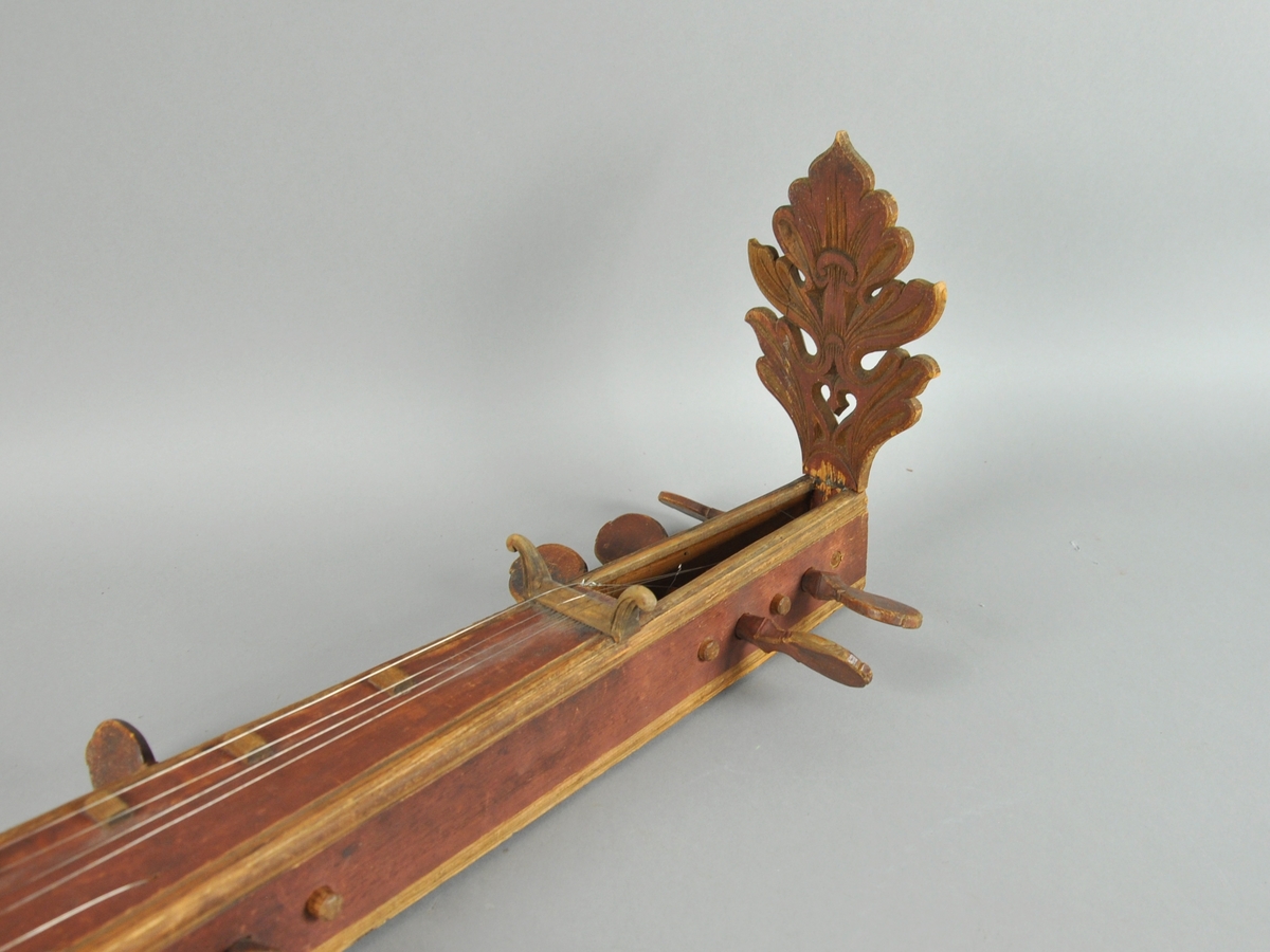 Langeleik av gudbrandsdalstype, med utskåret endestykke som har en inskripsjon på baksiden. Åtte strengeskruer av tre, hvorav den ene er brukket. Utskåret rose midt på kassen.