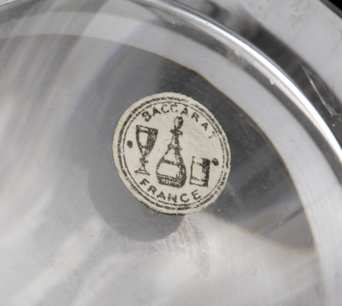 Dricksglas med slipade facetter runt om. Kantig botten.
Etikett undertill: Rund med två svarta ringar; i mitten vinglas, karaff och dricksglas. "Baccarat France"