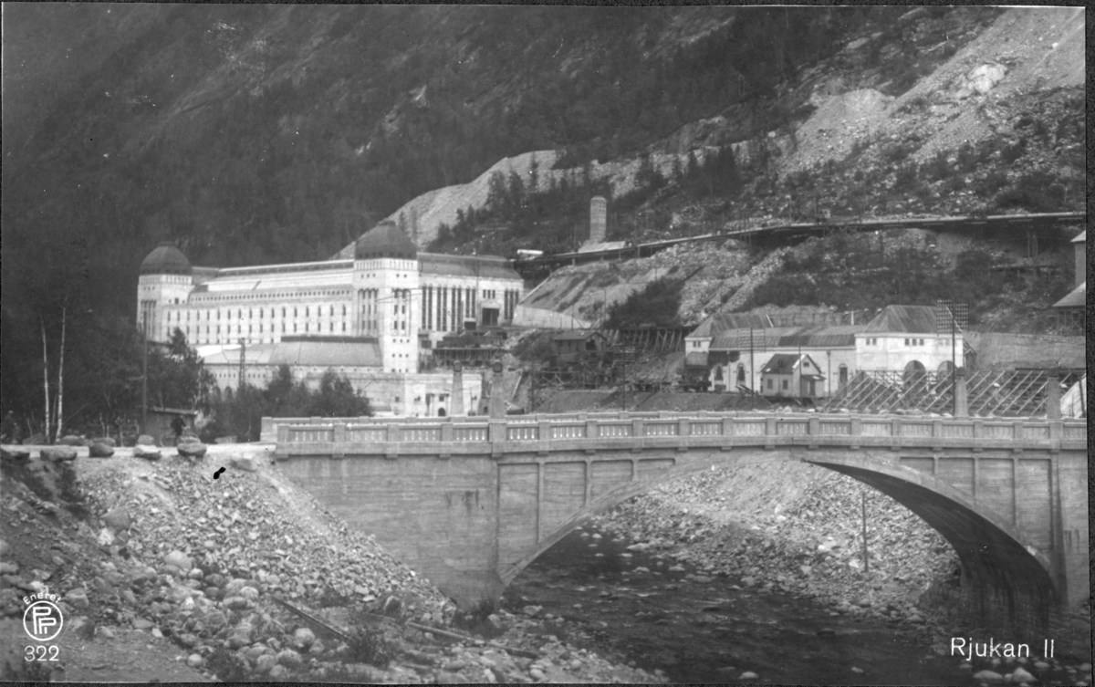 Fra nordvest, med bro i forgrunnen. Postkort fra Oppi forlag 332. Udatert. Bilder etter Trygve Bakke som var ingeniørutdannet på NTH, bygningslinjen, med eksamen i 1918. Deretter arbeidet han ved Vittingfoss kraftanlegg og Vestfold Kraftselskap i 1919-1922. I Oslo Boligdirektorat 1923-31 og fra 1932 i Oslo Vann- og kloakkvesen. (Iflg hans egne opplysninger i Vi fra NTH - De første 10 kull, 1933)..Hans eventuelle tilknytning til NVE er ukjent, likeså bakgrunnen for at albumet er kommet hit..