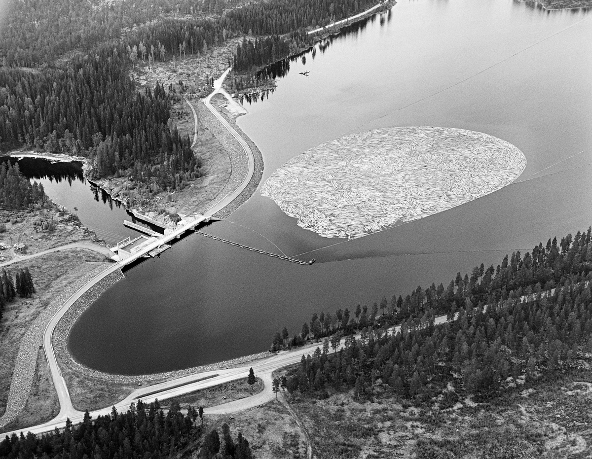 Flyfotografi av tømmerbom i den ytre (sørvestre) enden av Løpsjøen, en oppdemt del av elva Søndre Rena i Åmot kommune i Hedmark.  Fotografiet er tatt i mai 1984, den siste sesongen det var tømmerfløting i denne delen av Glommavassdraget.  Løstømmer fra områder høyere oppe i vassdraget var altså samlet i en ringbom av sammenkjedete tømmerstokker, som i sin tur er omgitt av ledelenser som skulle forebygge at tømmeret la seg mot land (strendene).  Vi skimter også ei lense som går vinkelrett ut fra damkonstruksjonen.  Den skulle bidra til at stokkene – når fløterne var klare for det – kunne slippes mot det såkalte «tømmerløpet» i dammen.  Dette er en kraftverksdam som utnytter vann fra Søndre Rena (inkludert vann som kommer i dette vassdraget fra Glomma via Rendalen kraftverk) og Søndre Osa.  Kraftverket er en fyllingsdam med flomløp og fisketrapp.  Fra åpningen i 1971 til fløtinga ble avviklet i 1984 hadde anlegget, som nevnt, også et tømmerløp.  Løpet kraftverk utnytter en fallhøyde på 19 meter.  Det er utstyrt med en kaplanturbin som yter 24 megawatt.  Øverst til høyre i bildet, langs Løpsjøens strandlinje, ser vi Fylkesveg 216 mellom Rena i Åmot og Jordet i Trysil, her kalt «Haugedalsvegen».  Vegen over damkrona var en samleveg for flere skogsbilveger i utmarka mellom Søndre Rena og Glomma, et område som etter åpningen av Rena leir i 1997 er blitt preget av militær aktivitet.