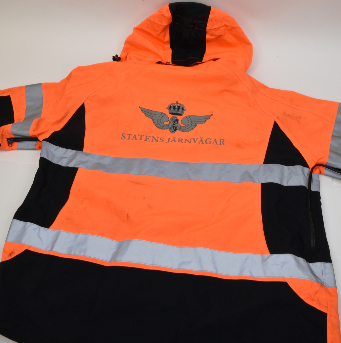 En arbetsjacka, varseljacka, storlek XL. Jackan är orange-aktig i färgen (typiska varselfärgen) och har två  reflexlinjer som går runt hela jackan. På slitytor som armbågar och rumpa har jackan svart textil. Jackan har tre dragkedje försedda fickor på utvändigt.