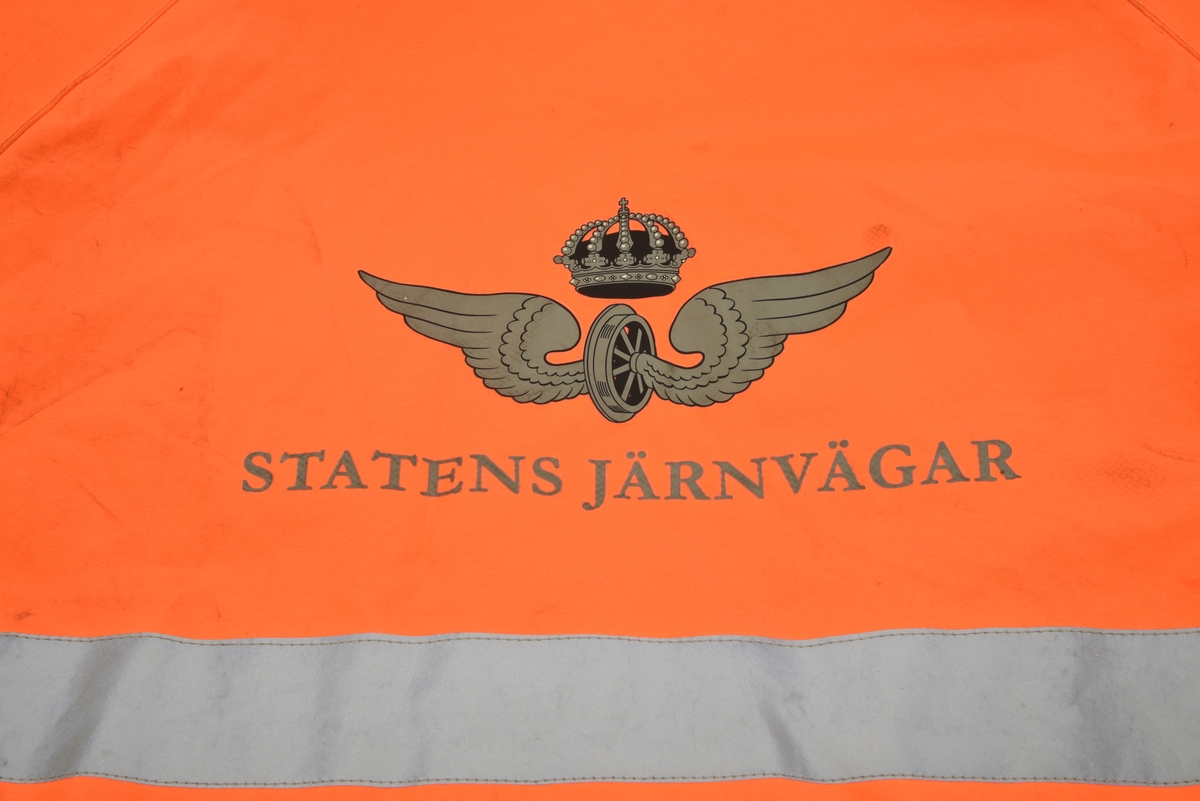 En arbetsjacka, varseljacka, storlek XL. Jackan är orange-aktig i färgen (typiska varselfärgen) och har två  reflexlinjer som går runt hela jackan. På slitytor som armbågar och rumpa har jackan svart textil. Jackan har tre dragkedje försedda fickor på utvändigt.