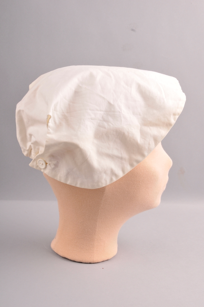Lerretshette sydd med maskin og for hand. Strikk og rynka midt bak. Eit knapphol på kvar side med knapp slik at hetta blir knept saman bak. Hetta er laga i eit stykke. Dobbelt tøy. Avrunda framme. Lapp med talet to i nakken.