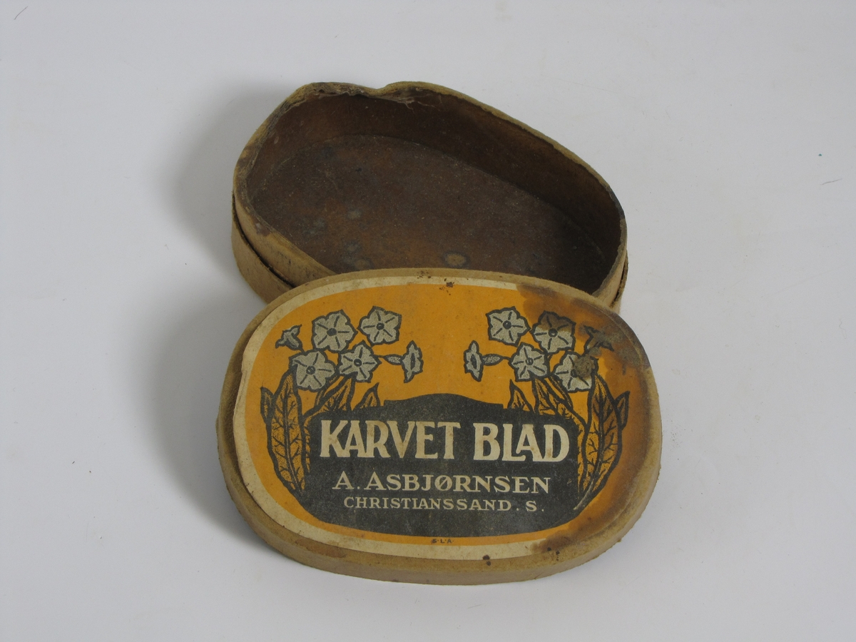 Tom tobakkseske i papp. Type "Karvet blad" fra A. Asbjørnsen, Christianssand S. Da den ble gitt til museet hadde den blitt brukt til oppbevaring av diverse småting (sikringer, sikkerhetsnål o.l.)