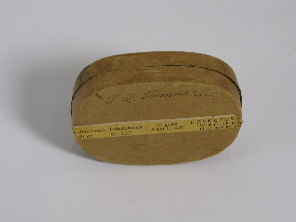 Tom tobakkseske i papp. Type "Karvet blad" fra A. Asbjørnsen, Christianssand S. Da den ble gitt til museet hadde den blitt brukt til oppbevaring av diverse småting (sikringer, sikkerhetsnål o.l.)
