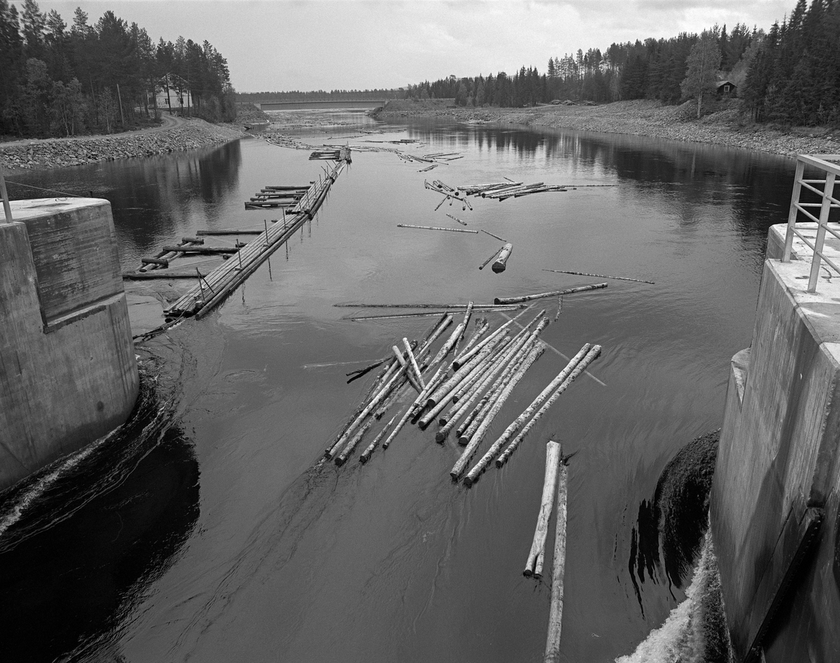 Fløtingstømmer på veg mot Osdammen der elva Søndre Osa renner ut fra Valmen, ei vik i den nordvestre enden av Osensjøen i Åmot i Hedmark. Fotografiet ble tatt i 1984, som var den siste fløtingssesongen i denne delen av Glommavassdraget. Tømmeret ble buksert hit fra ved hjelp av en slepebåt og sluppet gjennom dammen for fløting via Søndre Osa og Rena mot Glomma. I bakgrunnen ser vi vegbrua der fylkesveg 562 (2158) krysser Valmen. Denne vegen går langs Osensjøens vestside.