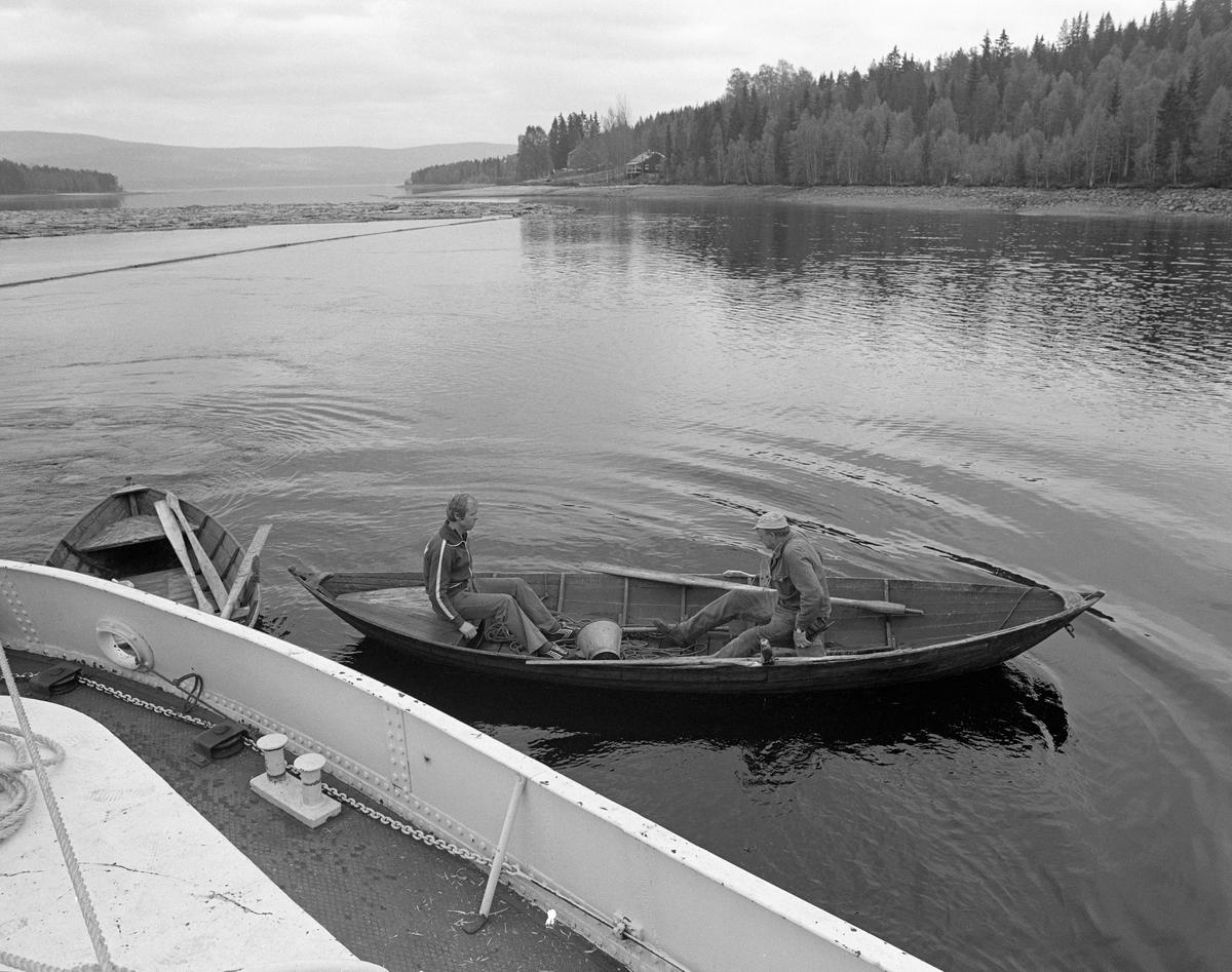 Fortøying av bom i Valmen, Osensjøen, Nordre Osen, Åmot kommune, Hedmark. Mai 1984. Til høyre: Nikolai Myrene fra Søre Osen, Trysil. Til venstre: Knut Stener, Osen, Åmot. Ombord på slepebåten Trysilknut. To av mannskapet. Robåt. Tømmerbom. Trysil-Knut.