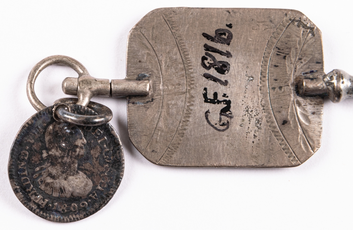 Urnyckel av silver, med vidhängande spanskt-colombianskt mynt (8 reales) från 1809, (Ferdinand Dei Gratia) också i silver. Nyckeln märkt E.S.H.