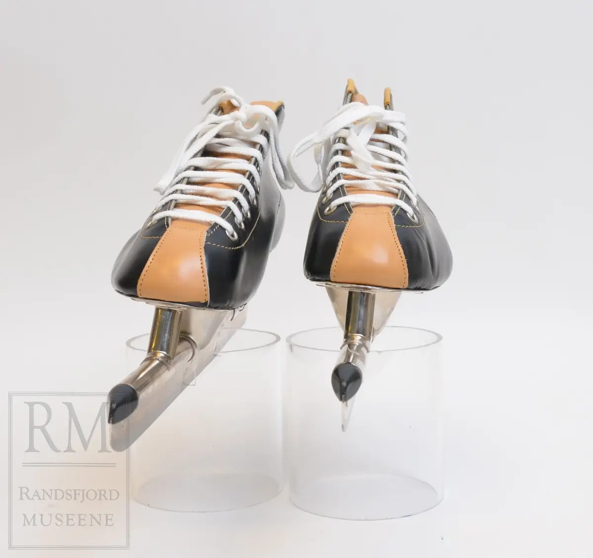 a-b) Skøyter: av svart skinn m / pløse og kant av beige skinn.Røret på skøytejernet avsluttet med plast i begge ender. 
c) plastpose til skøytene.
d) plaststykke.
e-f) Pappeske m/lokk. Brun papp med svart trykk på lokket.
g) pusseklut)
h) skøytefett i tube.