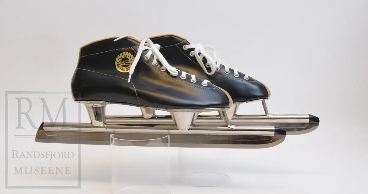 a-b) Skøyter: av svart skinn m / pløse og kant av beige skinn.Røret på skøytejernet avsluttet med plast i begge ender. 
c) plastpose til skøytene.
d) plaststykke.
e-f) Pappeske m/lokk. Brun papp med svart trykk på lokket.
g) pusseklut)
h) skøytefett i tube.