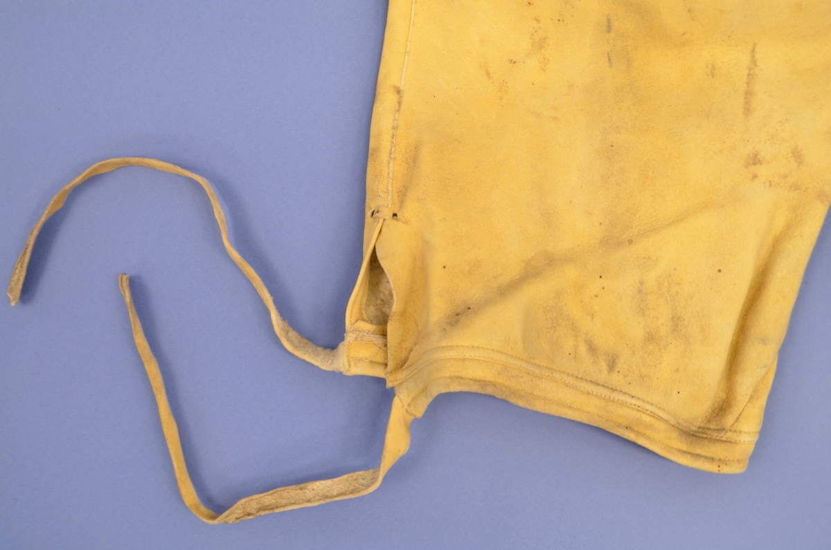 Knebukse i gult semska skinn med vanleg opning (gylf) midt framme. Påsydd lining som er fòra med bomull, linninga går ikkje heilt saman midt bak. Knappehol og knapp. Ein knapp i gylfen. Linning også under kneet, med skinnsnorer til å knyte saman linninga med. Ingen lommer. Ca 13 cm høgre midt bak.
