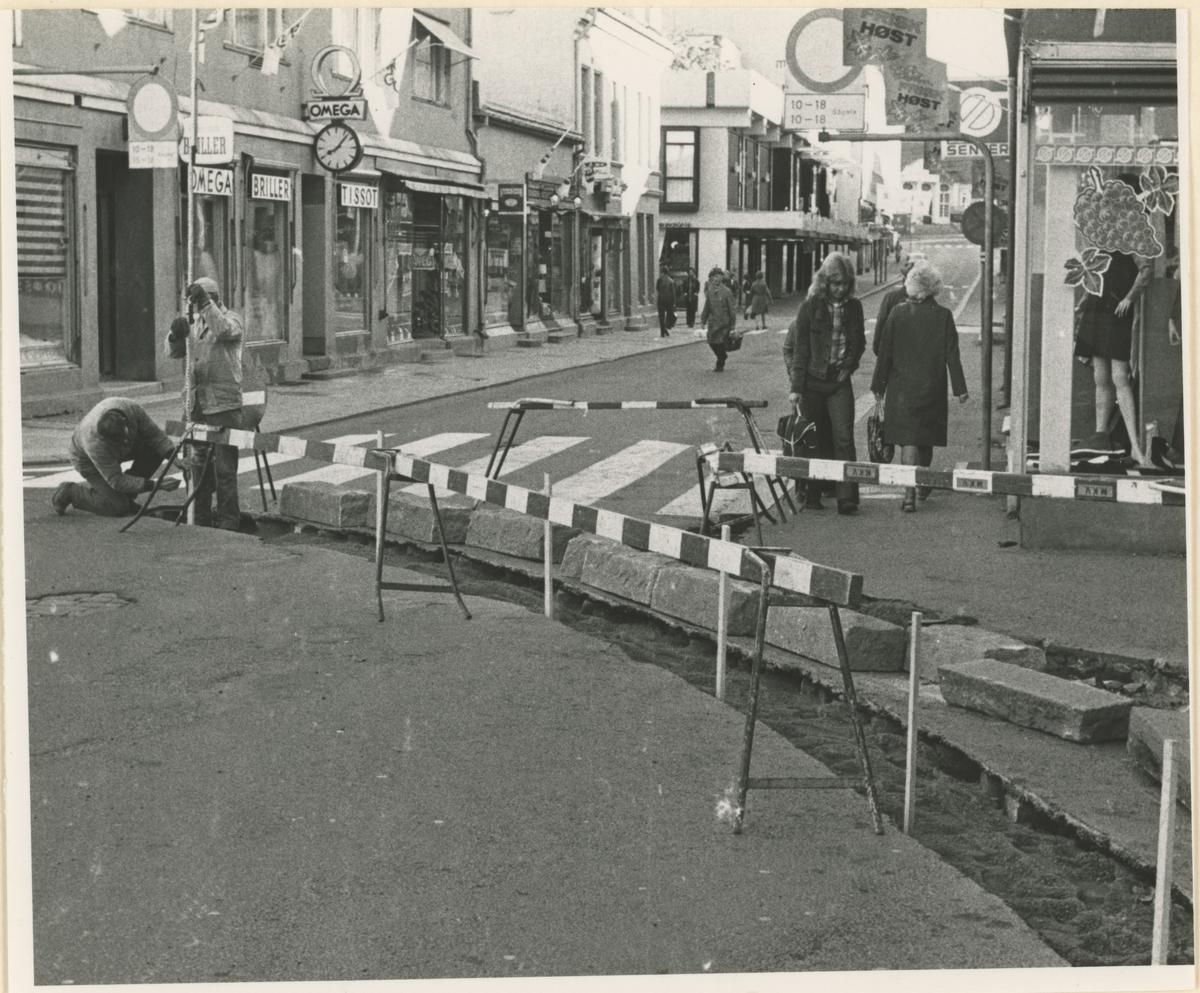 Bilde 1:
Fotograf har stått midt i Dronningens gate.
Detaljer: EPA til venstre og Møllhausen. På høyre side urmaker og klær.
Historikk: Banner: Ja til EF (EU). Resultat av valget ble NEI.

Bilde 2:
Fotograf har stått ved krysset Ibsens gate.
Detaljer: Arbeidere, folk, butikker.
Historikk: Det legges kantstein som skulle markere enveiskjøring.