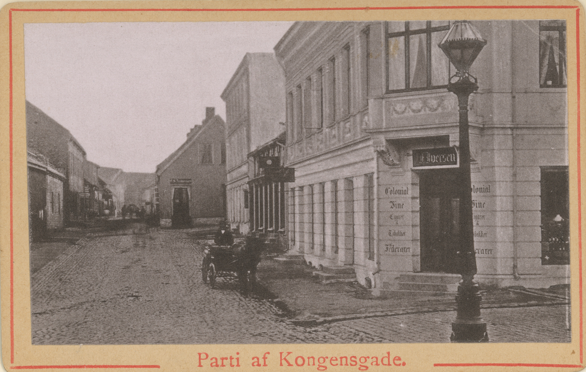 Før 1890. Fotograf har stått ved Øvre torv.
Detaljer:	Kongens gate 24, 22 og 20 med gamle 18 til høyre.
Historikk: Alle de bakre bygningene er revet og endret i dag.
Tekst under bildet: "Parti af Kongensgade".