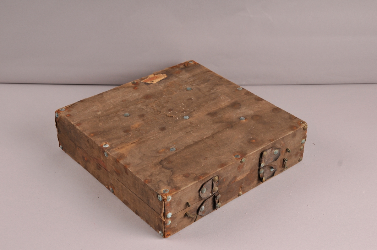 Koffert av tre, kledd med raudt tøy inni. Kofferten er inndela i 11 rom med 6 stk brynesteinar liggande i.