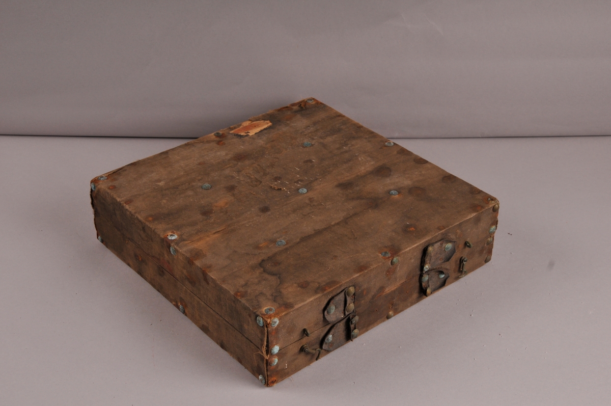 Koffert av tre, kledd med raudt tøy inni. Kofferten er inndela i 11 rom med 6 stk brynesteinar liggande i.