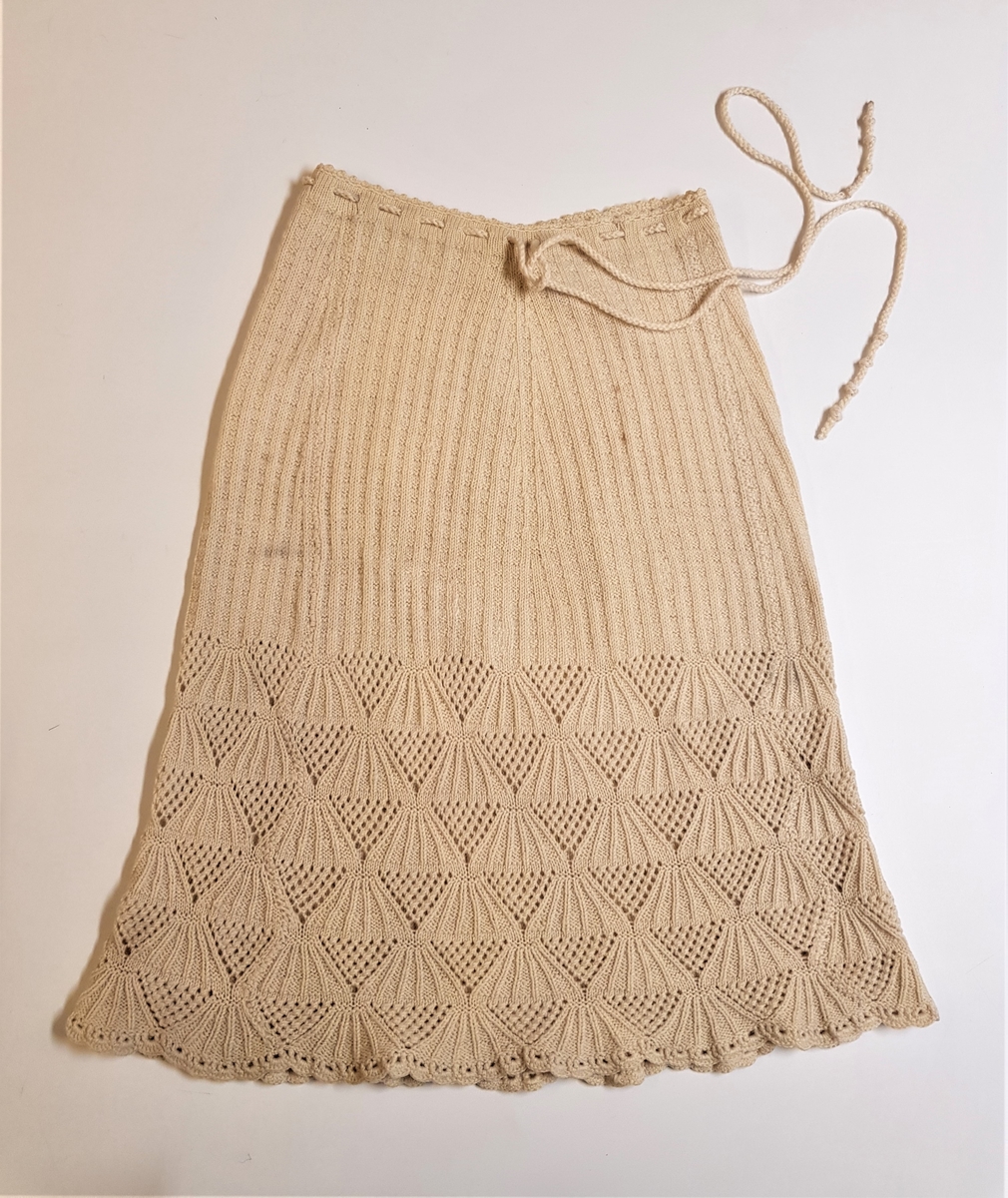 Smalt, men lett utskrådd underskjørt, strikket av gulhvit ullgarn. Hullrad med tvunnet ullsnor i livet, og "stripestrikket" ned til den nedre delen, der skjørtet avsluttes med et bredt parti mønsterstrikket, viftelignende mønster, kantet ytters med en hullbord. Skjørtet har vært omsydd og har søm midt bak med rikelig sømmonn. Sømmen når ned til det viftemønstrede partiet. Skjørtet har også vært sydd inn foran, på hver side, men disse sømmene er smale og gjennomgående helt ned. Pga det vifteformede mønsteret, er sømmene sydd for hånd slik at de følger mønsterets form og ikke bryter vifteformen. Se bildene.