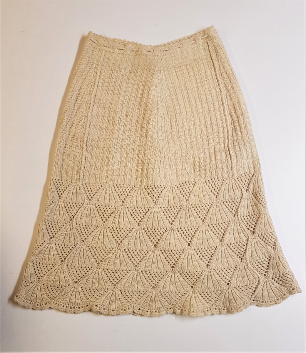 Smalt, men lett utskrådd underskjørt, strikket av gulhvit ullgarn. Hullrad med tvunnet ullsnor i livet, og "stripestrikket" ned til den nedre delen, der skjørtet avsluttes med et bredt parti mønsterstrikket, viftelignende mønster, kantet ytters med en hullbord. Skjørtet har vært omsydd og har søm midt bak med rikelig sømmonn. Sømmen når ned til det viftemønstrede partiet. Skjørtet har også vært sydd inn foran, på hver side, men disse sømmene er smale og gjennomgående helt ned. Pga det vifteformede mønsteret, er sømmene sydd for hånd slik at de følger mønsterets form og ikke bryter vifteformen. Se bildene.