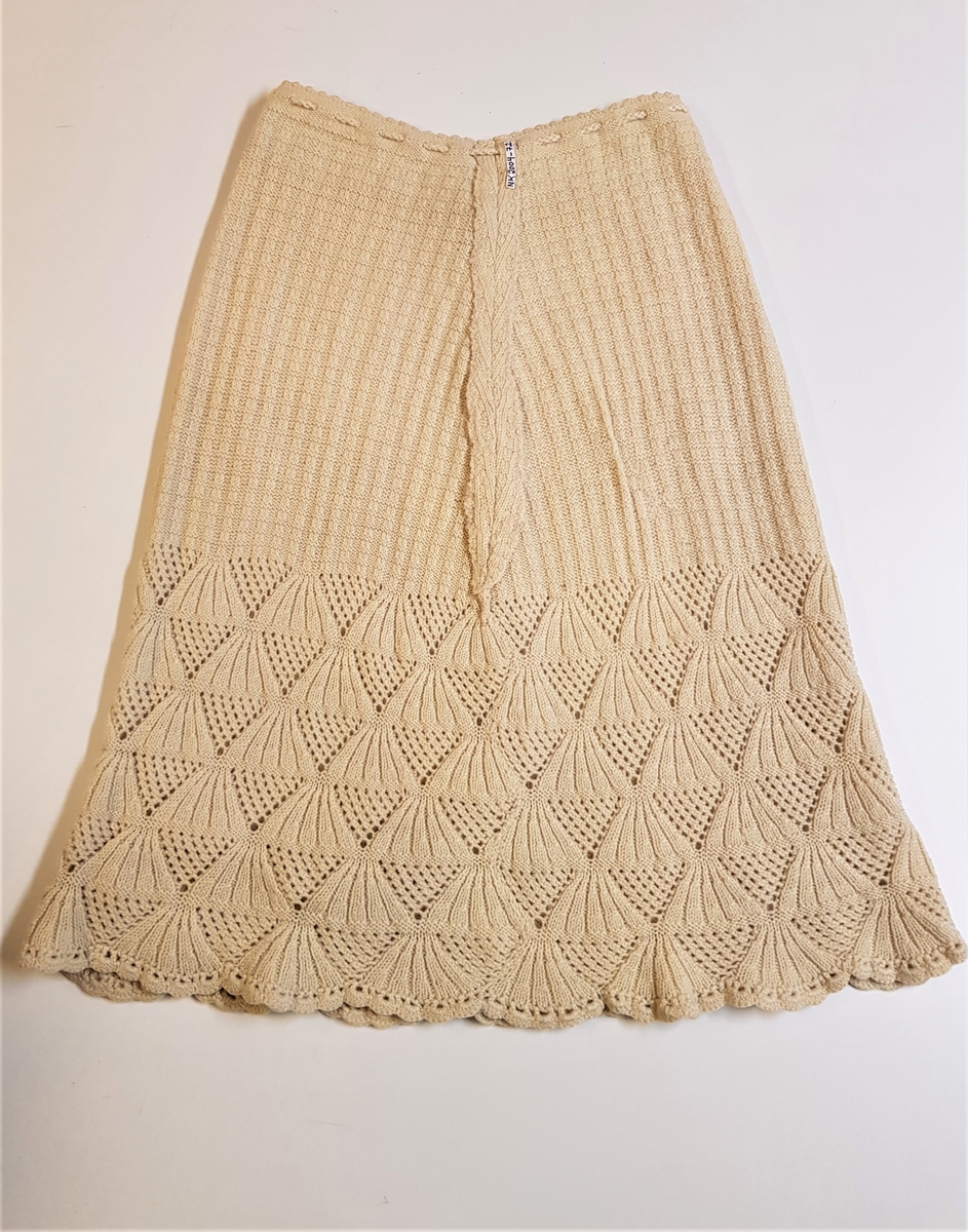 Smalt, men lett utskrådd underskjørt, strikket av gulhvit ullgarn. Hullrad med tvunnet ullsnor i livet, og "stripestrikket" ned til den nedre delen, der skjørtet avsluttes med et bredt parti mønsterstrikket, viftelignende mønster, kantet ytters med en hullbord. Skjørtet har vært omsydd og har søm midt bak med rikelig sømmonn. Sømmen når ned til det viftemønstrede partiet. Skjørtet har også vært sydd inn foran, på hver side, men disse sømmene er smale og gjennomgående helt ned. Pga det vifteformede mønsteret, er sømmene sydd for hånd slik at de følger mønsterets form og ikke bryter vifteformen. Se bildene.