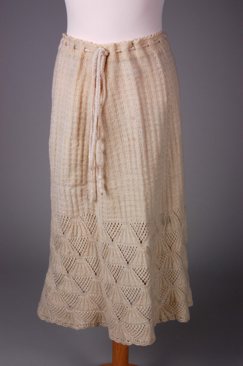 Smalt, men lett utskrådd underskjørt, strikket av gulhvit ullgarn. Hullrad med tvunnet ullsnor i livet, og "stripestrikket" ned til den nedre delen, der skjørtet avsluttes med et bredt parti mønsterstrikket, viftelignende mønster, kantet ytters med en hullbord. Skjørtet har vært omsydd og har søm midt bak med rikelig sømmonn. Sømmen når ned til det viftemønstrede partiet. Skjørtet har også vært sydd inn foran, på hver side, men disse sømmene er smale og gjennomgående helt ned. Pga det vifteformede mønsteret, er sømmene sydd for hånd slik at de følger mønsterets form og ikke bryter vifteformen. Se bildene.