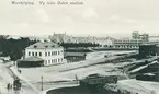 Vykort med motiv över stationsområdet vid Norrköpings Östra station. Stationen stod klar 1893 och var utgångspunkt för järnvägstrafiken ut mot slutstationerna Arkösund respektive Valdemarsvik. Bortom stationsbyggnaden ses Östra promenaden, där den äldre bebyggelsen kontrasterar mot det nyligen färdigställda tryckeriet Lithografen, ritad av Carl Bergsten. Vy mot nordväst.