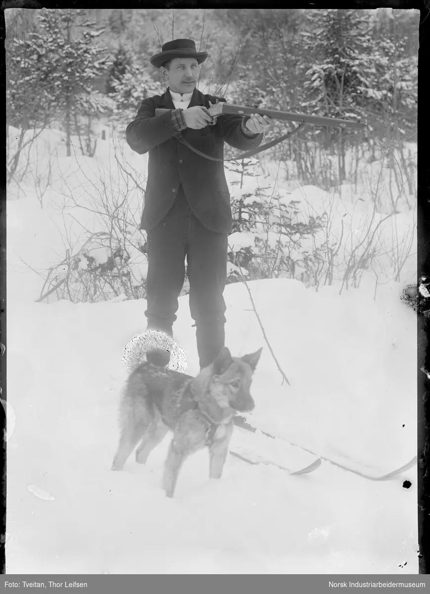 Jeger med gevær, ski og hund oppstilt.