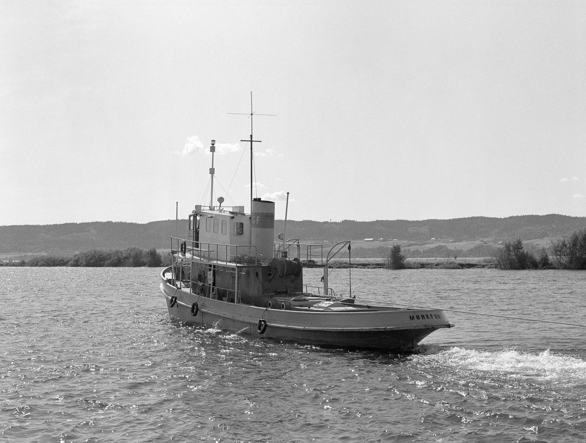 MB Mørkfos, fotografert under tømmersleping på innsjøen Øyeren, antakelig i 1985, det siste året det foregikk kommersiell tømmerfløting i Glommavassdraget.  Båten er 72 fot lang og 14 fot Fotografiet er tatt skrått bakfra.  Vi ser slepelina, en lang vaier som ble brukt til å dra et slep med tømmer som var «soppet» (buntet) og bundet sammen sørover innsjøen.  Sjølve slepet ser vi ikke på dette fotografiet, for det var viktig med en viss avstand mellom «propellvannet», det opprørte vannet bak båten og tømmeret.  Ble avstanden for kort ville strømmen fra propellene øve for kraftig press på tømmeret i gal retning.  Fotografiet er tatt på den øvre delen av slepestrekningen, i deltaområdet nedenfor lenseanlegget.  Her var det grunt farvann, og båten og slepene måtte følge en meandrerende djupål og ha bistand fra den noe mindre slepebåten Rauma, som bisto med bukseringa av den bakre enden av slepet.  Dette var et vanskelig «slalåmløp» som tok om lag fire timer.  Skipperne på båtene hadde telefonforbindelse.  Slik arbeidet man seg langsomt og forsiktig ned til Sofiedal, et lite bruk på Øyerens vestside, like ved grensa mellom Rælingen og Enebakk kommuner i Akershus.  Herfra kunne Mørkfos aleine gå videre nedover mot Sleppetangen og Glommas videre løp.  På denne strekningen kunne Mørkfos trekke to slep av den størrelsen det var mulig å få med ned gjennom deltaområdet.