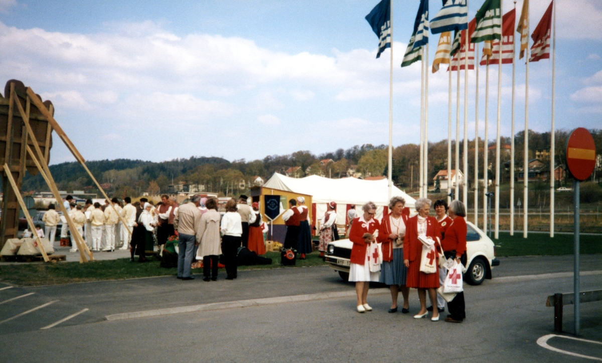 Röda Korsets insamling "En miljon träd" på Ikeas parkeringsplats år 1985. Till höger ses fem kvinnor hållandes Röda Korset-kassar. Bakom dem skymtas ett tält. I bakgrunden till vänster ses ungdomar från Musikskolan, klädda i gul överdel och vita byxor, som spelade under dagen.