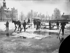 Isupptagning på Svartån vid Järnvägsbron.
3 män med issågar, 5 män med isstänger. 2 hästar med varsin flaksläde. 
Till vänster i fonden syns del av Villa Fridå, Västra Bangatan 1, byggmästare Per Erikssons bostad. Till vänster om villan låg hans och brodern Israels snickeriverkstad, Bröderna Erikssons snickerifabrik.