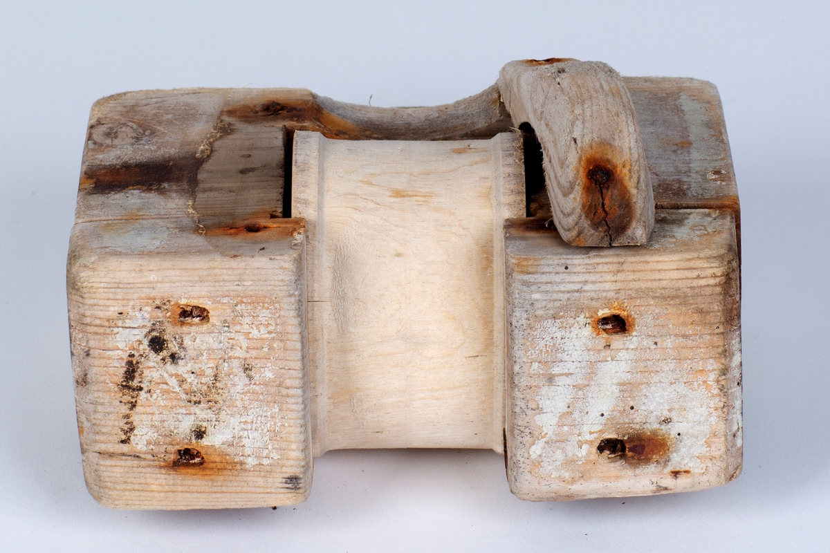 En firkantet tregjenstand med en trommel i midten som går rundt. Satt sammen med spiker.