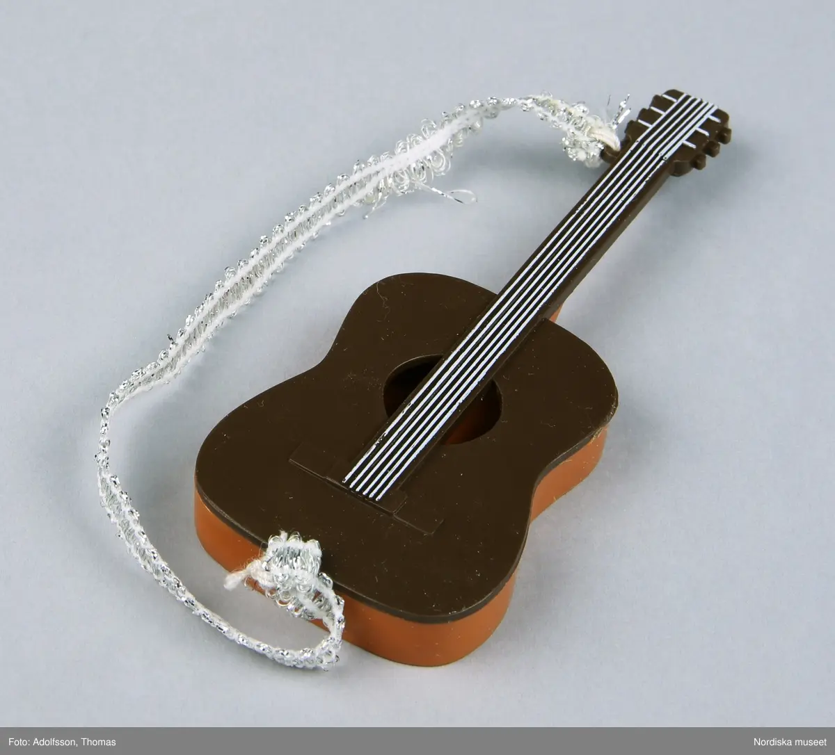 a-b) Två likadana dockgitarrer av plast med ett silverfärgat band av syntet. Den ena hör till dockan Benny, NM0334232 a-e. och den andra till Björn, NM0334233 a-d.