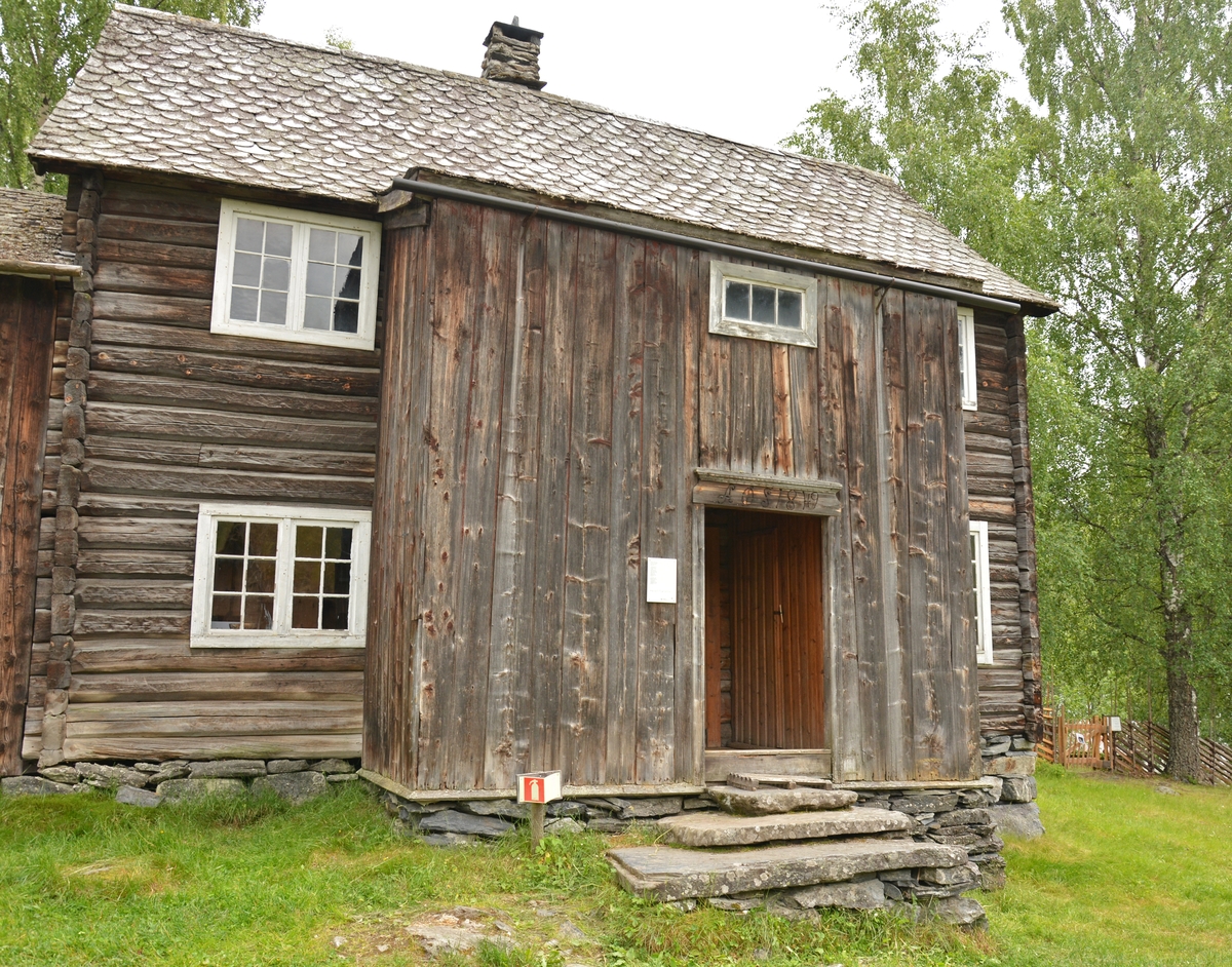 Bygning i to høgder, med sval og rosemåla dører.