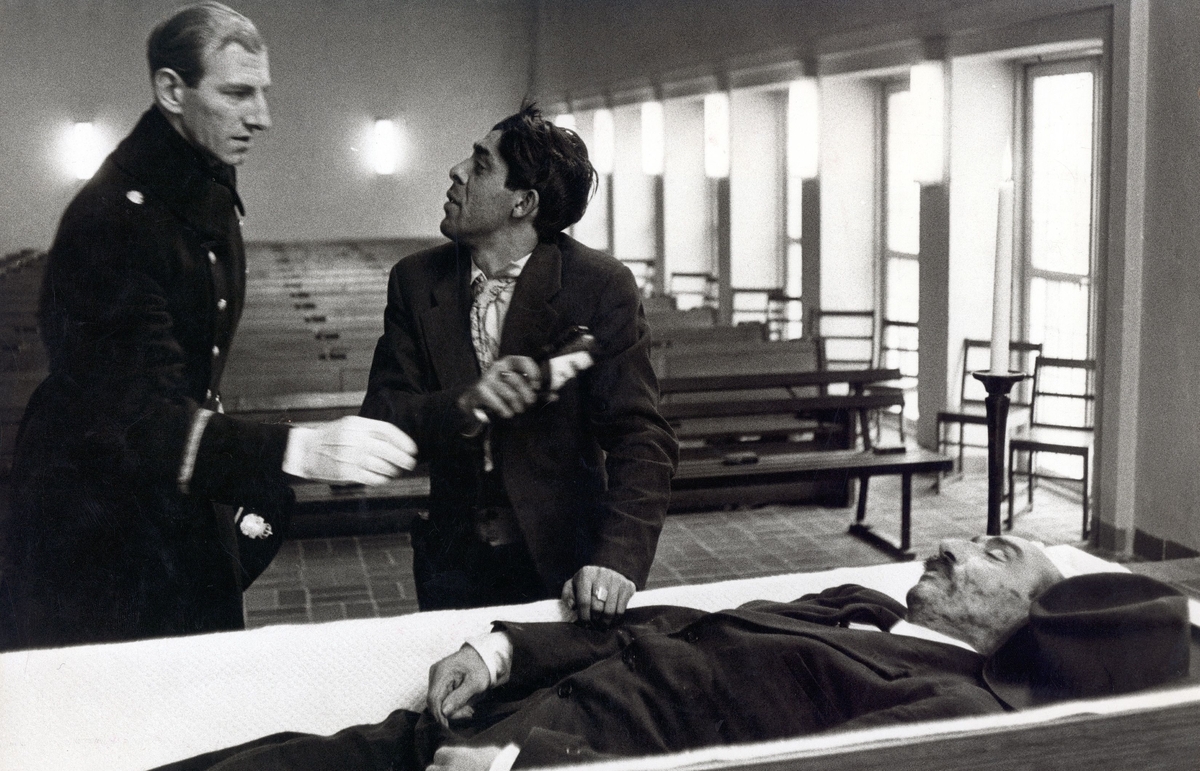 En romsk man önskar lägga med en pilsnerflaska i sin fars kista inför hans begravning. En polis intill honom försöker hindra honom.  
Årets bild 1958, tagen i Stillhetens kapell (tid. Uppståndelsens kapell) i Karlstad. Sonen vill lägga en flaska pilsner i sin fars kista för att ta med på vägen till himlen.