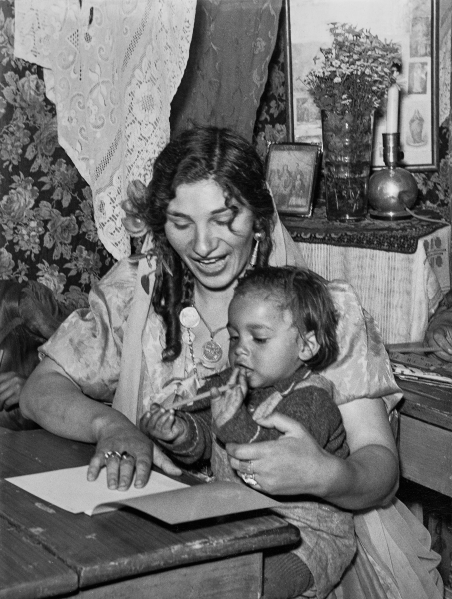 En romsk mamma sitter i skolbänken med sin lille i famnen för att gå i sommarskola 1943.