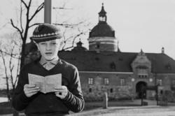 En pojke står med sin betygsbok i händerna och ser in i kame