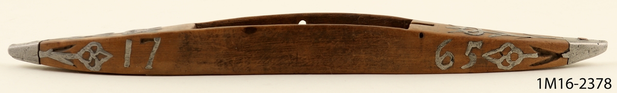 Vävskyttel med ornament av metall samt årtalet 1765.