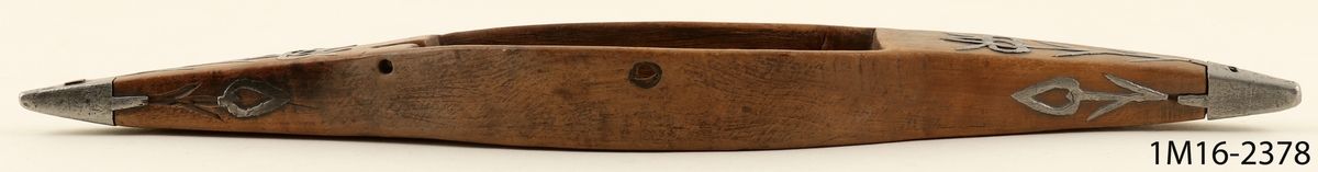 Vävskyttel med ornament av metall samt årtalet 1765.